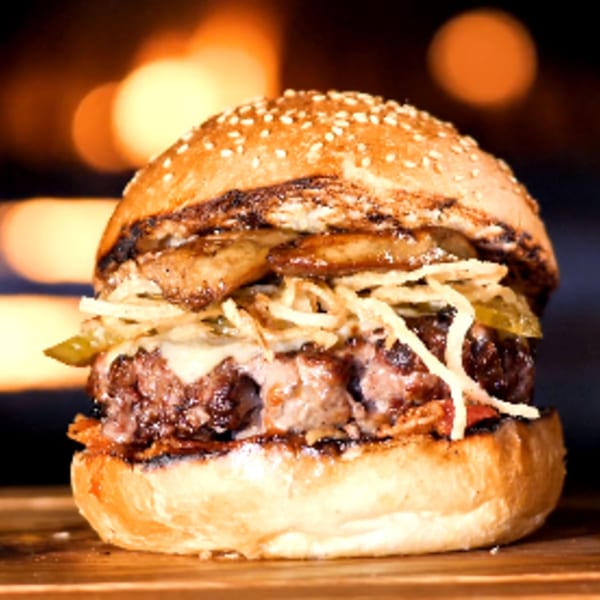 Gourmet burger with melted cheese, crispy onions, and pickles on a sesame seed bun.