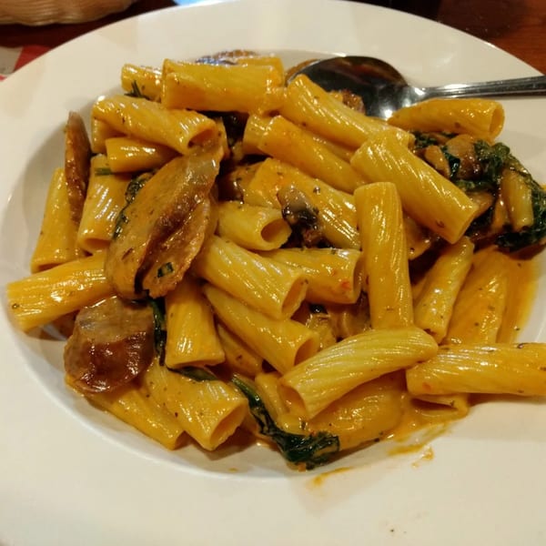 Rigatoni pasta with sausage, spinach, and a creamy orange sauce on a white plate.